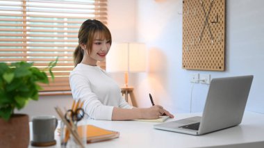 Attractive young woman watching online webinar on laptop computer during remote working from home.