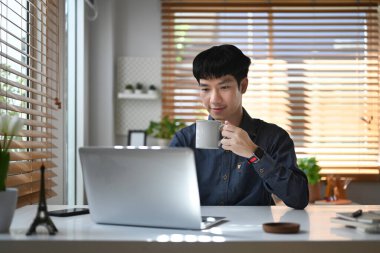 Asian businessman drinking coffee and checking email or reading online news on laptop at the morning.