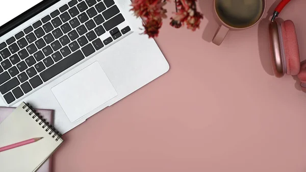 Feminine workspace with laptop, blank notepad, wireless headphone and coffee cup. Top view with copy space.