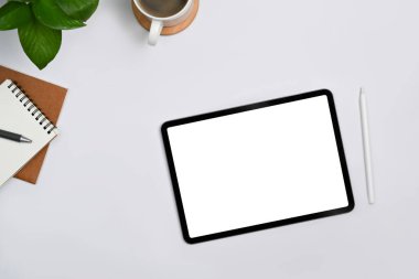 Digital tablet with empty display, stylus pen, coffee cup and notebooks on white office desk. Top view, Flat lay.