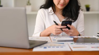 Female office worker sitting front of laptop and chatting online on smart phone.