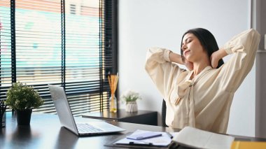Female employee relaxing at work, reclining back in chair and stretching her arms.