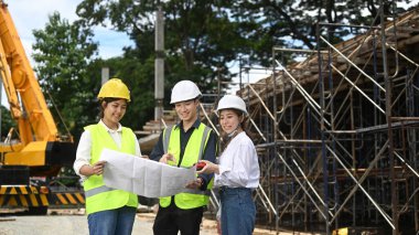Team of civil engineer and specialists inspect commercial, industrial building construction site with crane in the background.