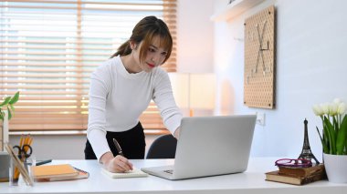 Charming young woman using laptop computer during remote working from home.