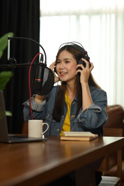 Young female content creator using microphone and headphones to recording vlog for her channel listeners.