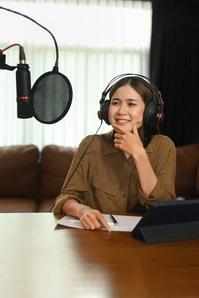 Positive female radio host listening to interesting conversation with guest during recording podcast in broadcasting home studio.