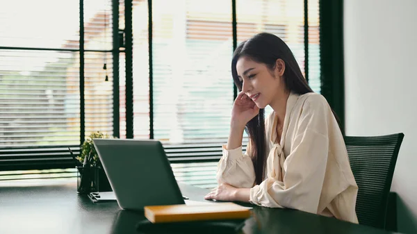 Gorgeous woman entrepreneur sitting in her contemporary office and checking information on laptop.