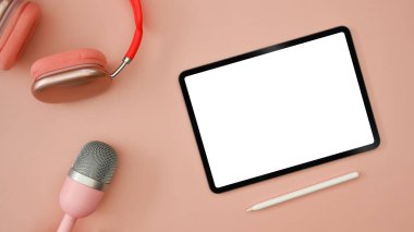 Flat lay digital tablet, wireless headphone and microphone on pink background. Radio, podcasts, blogging and technology concept.