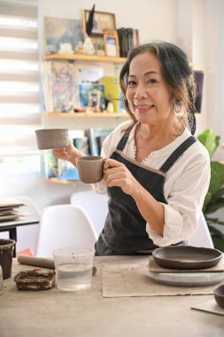 Professional mature ceramist making handicraft crockery in her workshop. Activity, handicraft, hobbies concept.