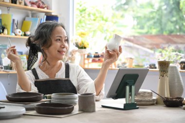 Satisfied mature woman enjoy creating handcrafted ceramics in pottery workshop.