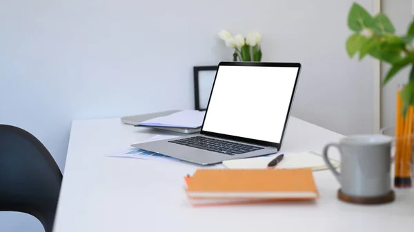 White office desk with laptop, potted plant, coffee cup and notebooks. Blank screen for your advertise text.