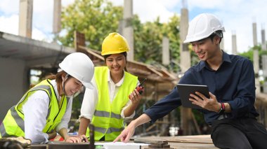 Civil engineer and architect in safety helmet are planning development details and inspecting industrial building construction site.
