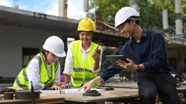 Architects and civil engineer inspecting and discussing project details together at construction site.