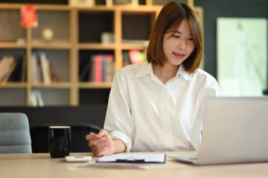 Asian woman creative designer working on new project, checking online information on her laptop.