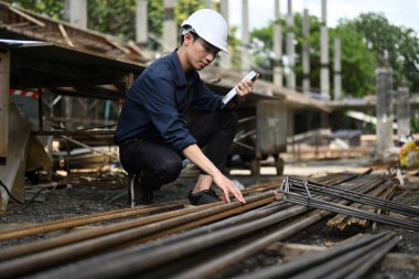 Young male inspectors wearing safety helmet check the quality of steel structure at industrial building construction site.