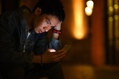 Young hipster man using mobile phone while walking through the night city streets. Night life concept. 