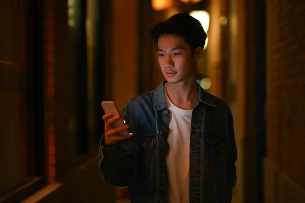 Young hipster man using mobile phone while walking through the night city streets. Night life concept.