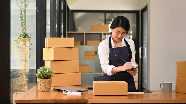 Young woman entrepreneur working in home office, preparing parcel boxes of product for delivery. Online selling, e-commerce concept.