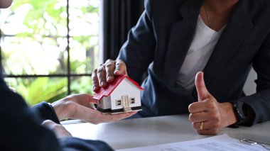 Cropped shot of businessman holding house model and showing thumb up sign approve excellent quality or mortgage offer.