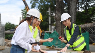 Team of civil engineer wearing safety helmet discussing project details at construction site.