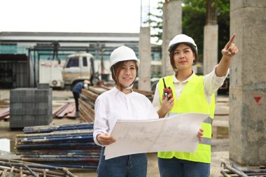 Female engineer manager and architect in helmet are planning development details and inspecting industrial building construction site.