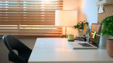 Comfortable home office with laptop , coffee cup, houseplant and supplies on white table.