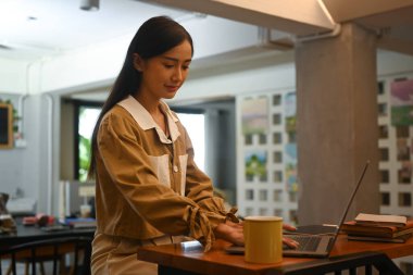 Young businesswoman sitting in contemporary coffee shop and using laptop computer.