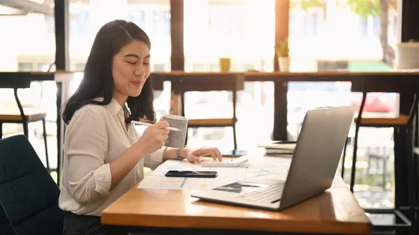 Cheerful Woman Office Worker Drinking Hot Coffee Using Laptop Computer — 스톡 사진