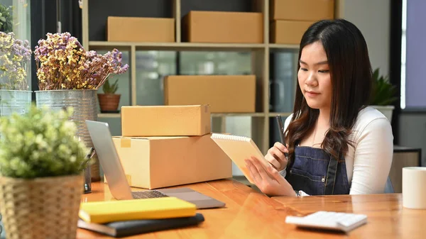 Young woman online seller checking product purchase order on digital tablet. E-Commerce, online business, online sales concept.