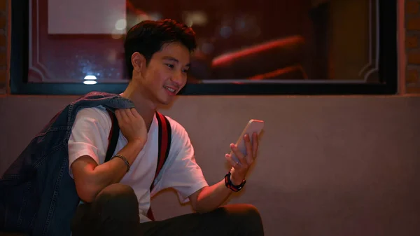 Handsome Asian Male Sitting Showcase Night City Street Using Mobile — Stock fotografie