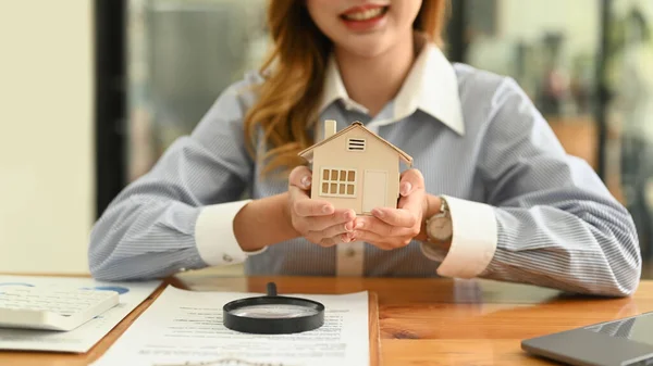 Happy young woman investor holding miniature house in her hands. Real estate investment, purchase and sale concept.