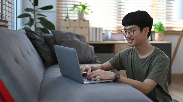 笑顔アジアの男は居心地の良いリビングルームに床に座って ラップトップで自宅から電子メールやオンラインで働く — ストック写真