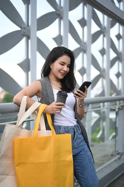 Alışveriş Torbalarıyla Şık Bir Kadın Modern Binanın Terasında Akıllı Telefonunu — Stok fotoğraf