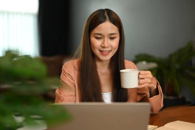 Kahve içen ve bilgisayarından iş e-postalarını kontrol eden çekici bir girişimci kadın..