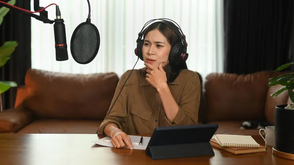 Concentrated female radio host listening to interesting conversation with guest during recording podcast in home studio.