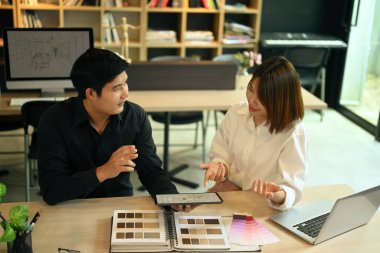 İki genç iç mimar, yaratıcı ofisteki ahşap masada dijital tablet ve renk paletiyle çalışarak proje planlıyorlar..