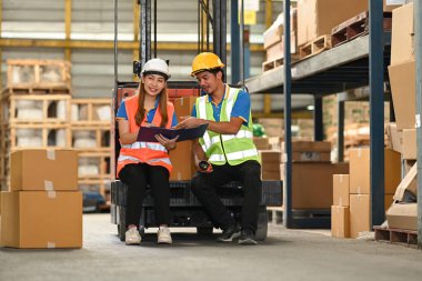 Depo çalışanları, forklift kamyonunda oturup yeni gelen malları büyük bir depoda kontrol ediyorlar..