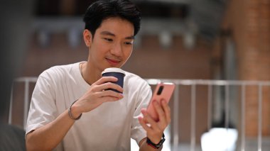 Yakışıklı Asyalı bir erkek gece kenti sokaklarında bankta oturuyor ve cep telefonuna mesaj yazıyor..