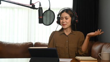 Gülümseyen genç kadın ev stüdyosunda dizüstü bilgisayar ve mikrofon kullanarak ses yayını yapıyor..