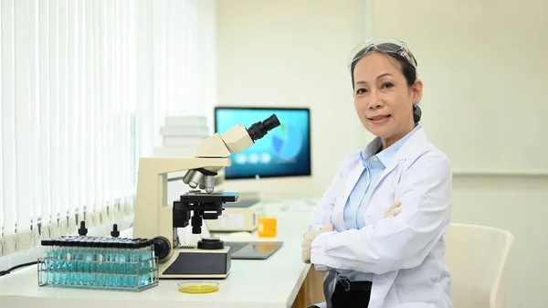 Medelålders Kvinna Klädd Vetenskapsman Uniform Sitter Med Armarna Korsade Laboratoriet — Stockfoto