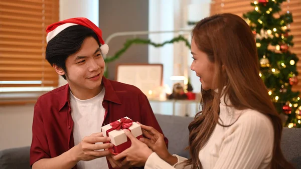 Young man giving surprise gift to his girlfriend during celebrating New Year at home. Family, holidays and people concept.