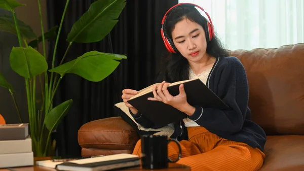 Ικανοποιημένη Νεαρή Γυναίκα Ακούγοντας Μουσική Ακουστικά Και Διαβάζοντας Βιβλίο Στον — Φωτογραφία Αρχείου