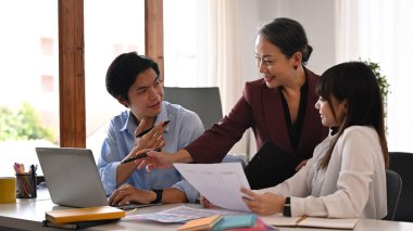 Gülümseyen orta yaşlı bayan yönetici genç çalışanlarla parlak ofiste yeni projeler tartışıyor..