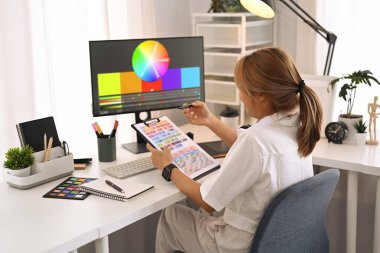 Renk paletiyle çalışan yaratıcı kadın modern grafik stüdyosunda tasarım projesi için renk örnekleri seçiyor..