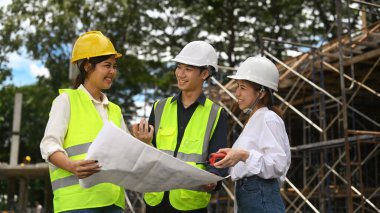 Güvenlik kaskı ve yansıtıcı ceketli mühendis ekibi endüstriyel inşaat projesinin ilerlemesini denetliyor..