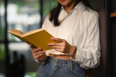 Kitap raflarının yanında durup kitap okuyan kırpılmış bir kız öğrenci. Halk, bilgi ve eğitim kavramı. 