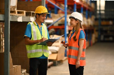Depo çalışanları, güvenlik üniforması içinde karton kutularda eşyalarla dolu bir depoda çalışıyorlar..
