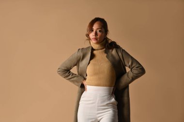 Sonbahar kıyafetli, bej arka planda poz veren güzel, şık bir kadın. Moda stüdyosu fotoğrafı, sonbahar moda ve güzellik konsepti..
