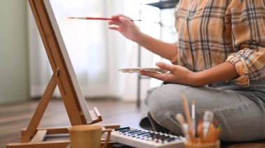 Kadın ressamın kırpılmış görüntüsü tuvalin önünde oturuyor ve suluboya ile resim yapıyor. Boş zaman aktivite konsepti.