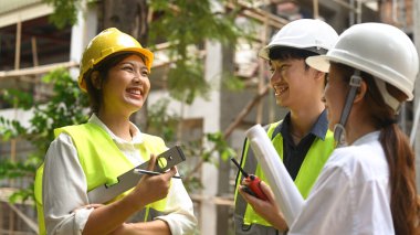 Güvenlik kaskındaki mühendis ekibi çalışma planını, inşaat alanında endüstriyel yapı tasarım projesini tartışıyor..